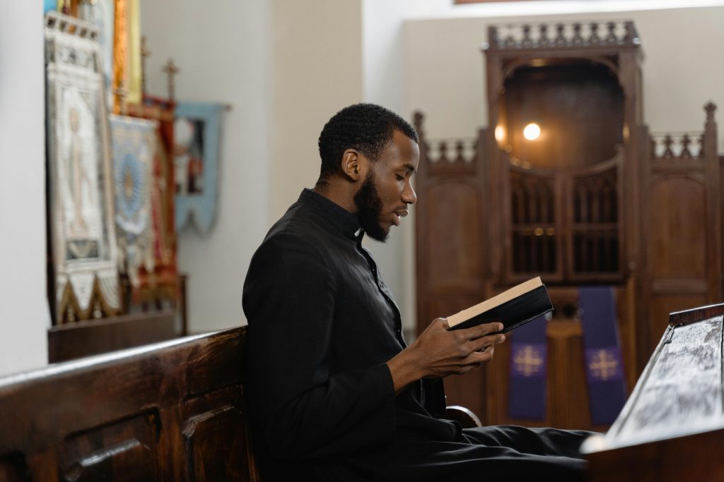 A priest immersed in reading the Bible while sitting in a church pew, capturing a serene spiritual moment.